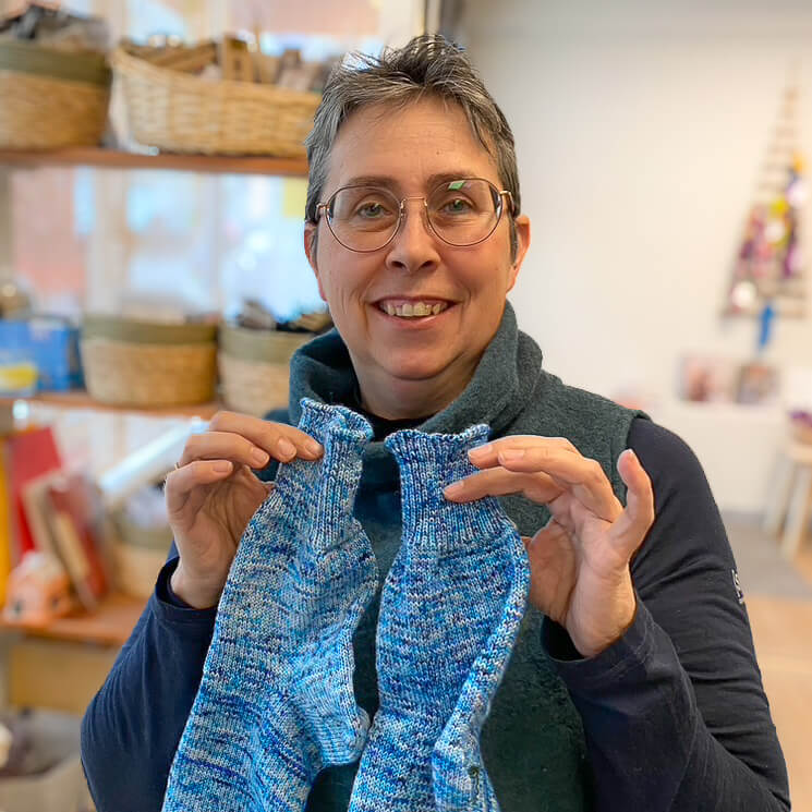 Portrait von Daniela Körner im Wollkorb in Pfullingen mit zwei blauen, selbstgestrickten Socken in der Hand