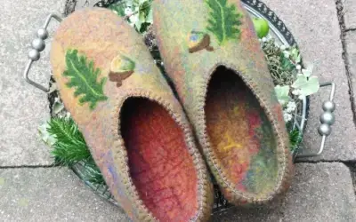 Ein paar gefilzte Hausschuhe, ähnlich wie Pantoffeln, innen bunt, außen graubraun mit gefilzten Blättern und Eicheln.
